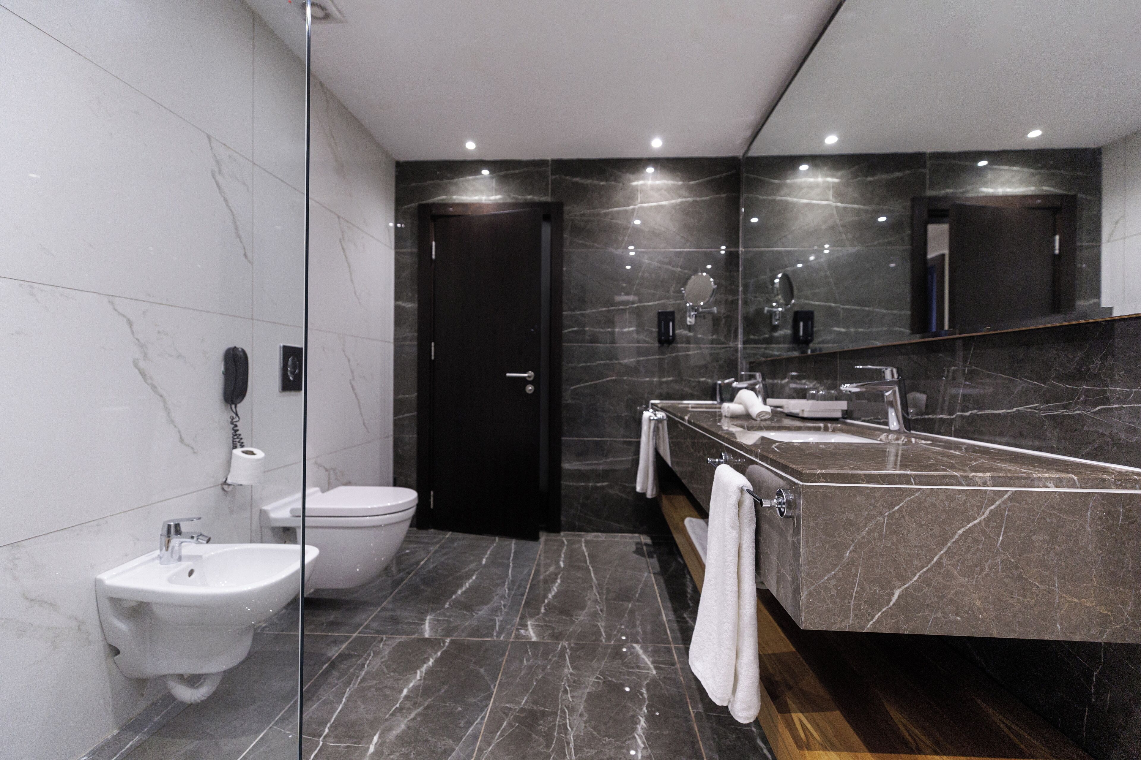 A modern bathroom with a bidet, toilet, and a large mirror above the sink.