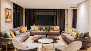 A modern living room with a sectional sofa, two armchairs, a coffee table, and a large window with curtains. - Riviera Royal Hotel (Conakry)