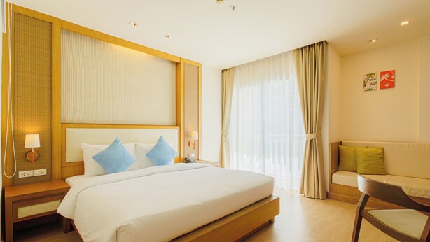 A modern hotel room with a large bed, a wooden nightstand, a bedside table, a chair, a sofa, and a large window with curtains. - ASHLEE Plaza Patong Hotel & Spa (Patong)