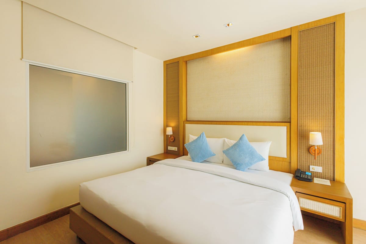 Ein Hotelzimmer mit einem großen Bett, einem Nachttisch mit Lampe, einem an der Wand montierten Fernseher und einer dekorativen Wandverkleidung.