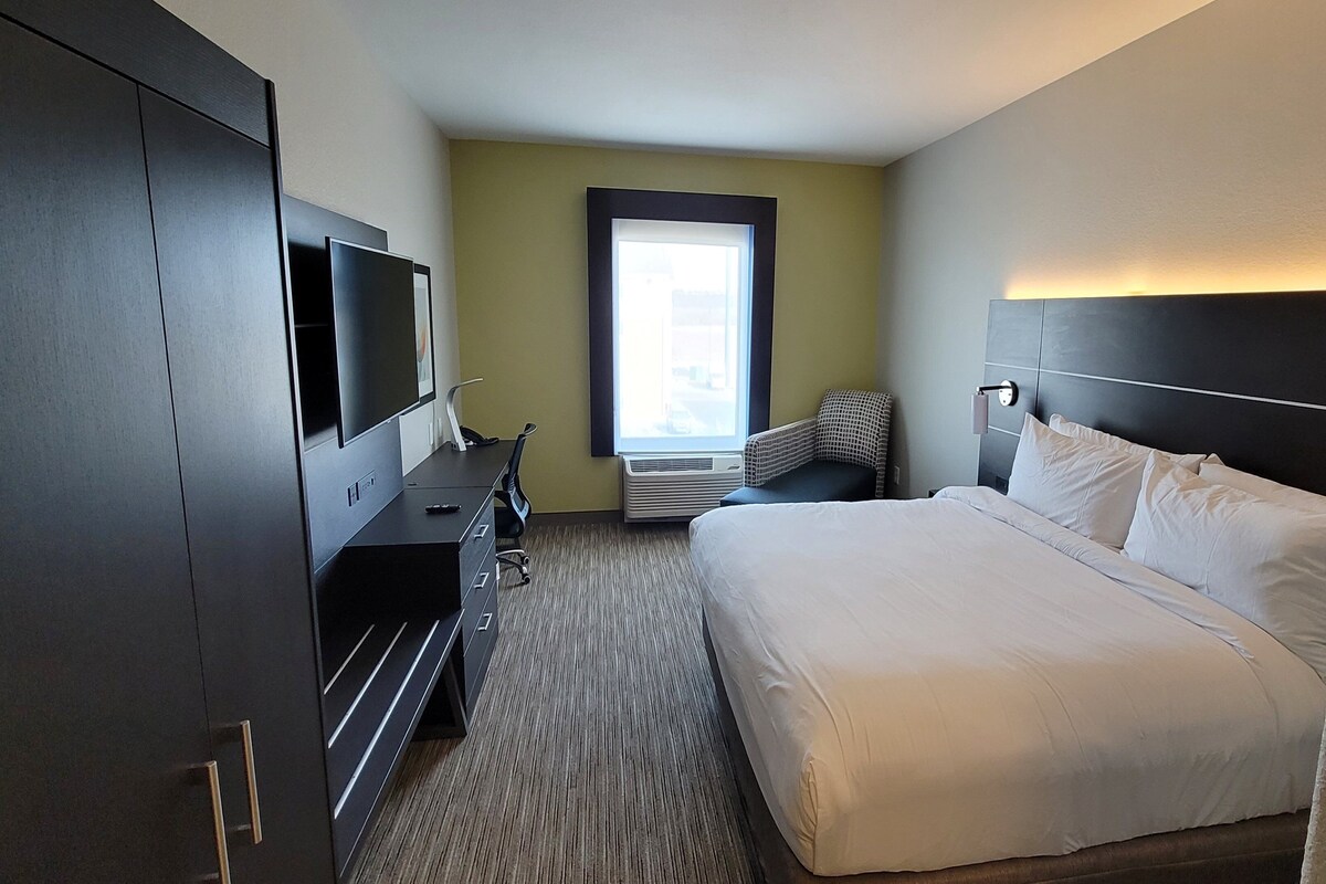 A hotel room with a large bed, a desk with a TV, a chair, and a window with a view of the outside.