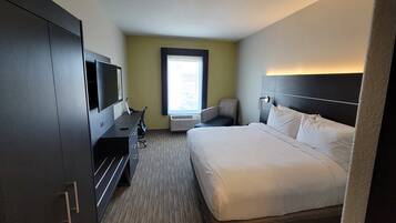 A hotel room with a bed, a desk with a television, a chair, and a window with a view.