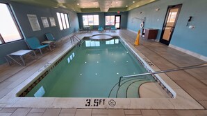 Une piscine intérieure d’une profondeur de 1,05 mètre, entourée de chaises longues et dotée d’un sol carrelé.