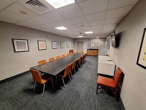 A conference room with a long table, orange chairs, framed artwork on the walls, and a kitchenette area. - Holiday Inn Express & Suites Junction City by IHG (Junction City)