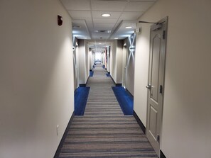 A hotel corridor with carpeted floors, doors on both sides, and overhead lighting.