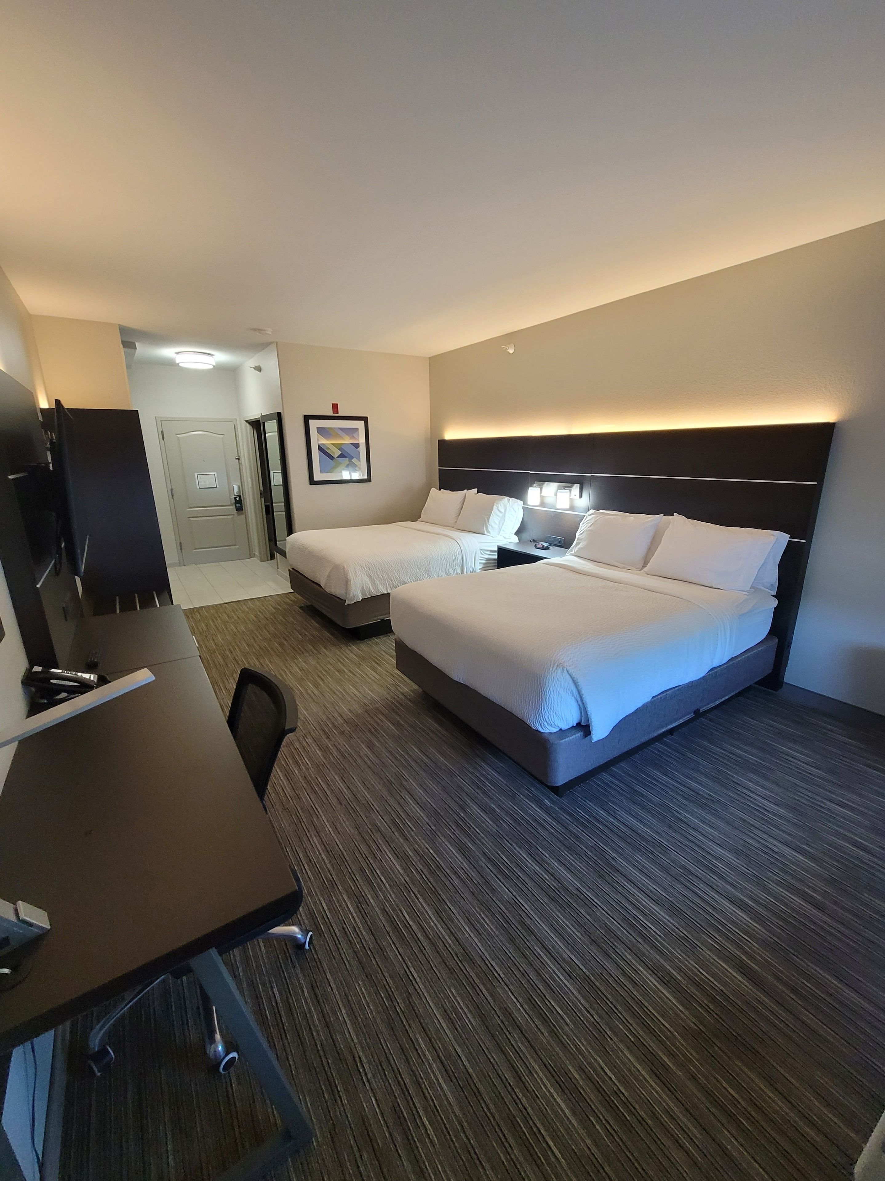 Habitación de hotel con dos camas, un escritorio, una silla, un televisor y un cuadro en la pared.