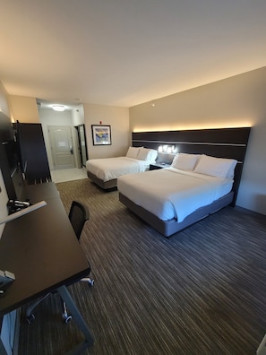 A hotel room with two beds, a desk, a chair, a TV, and a framed picture on the wall.