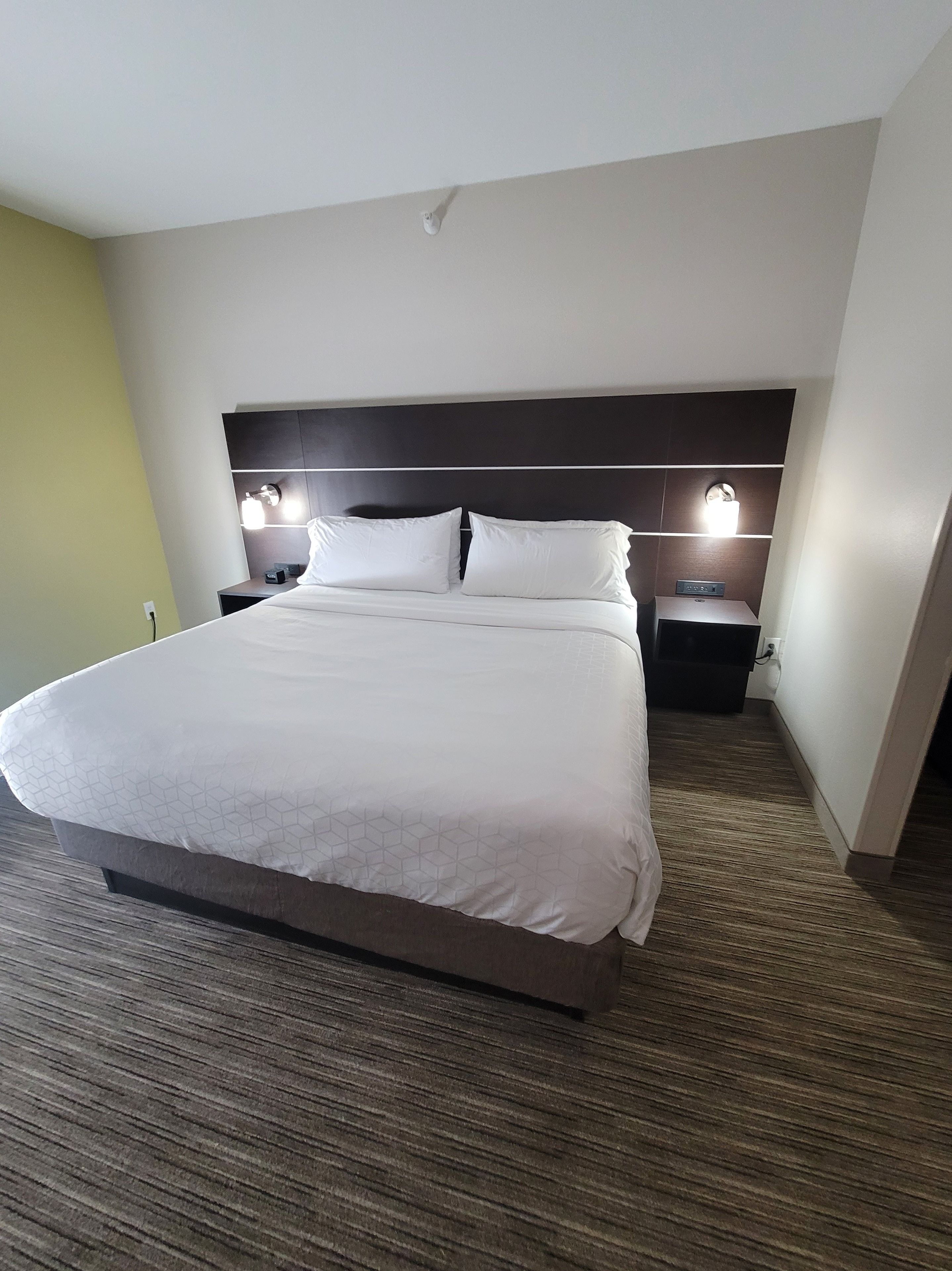 A hotel room with a large bed, two bedside tables, and a headboard with built-in lighting.
