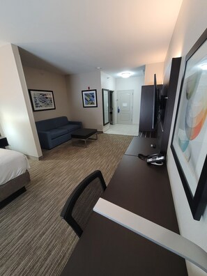 Una habitación de hotel con cama, escritorio, silla, sofá, televisor y puerta.