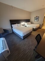 Habitación de hotel con dos camas, un escritorio, una silla y aire acondicionado instalado en la pared.