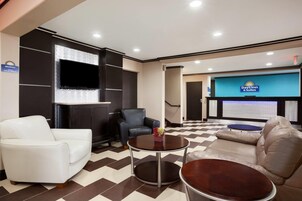 Un vestíbulo de hotel con piso a cuadros, un televisor de pantalla plana, un sofá blanco, un sillón de cuero y una pequeña mesa con un florero.