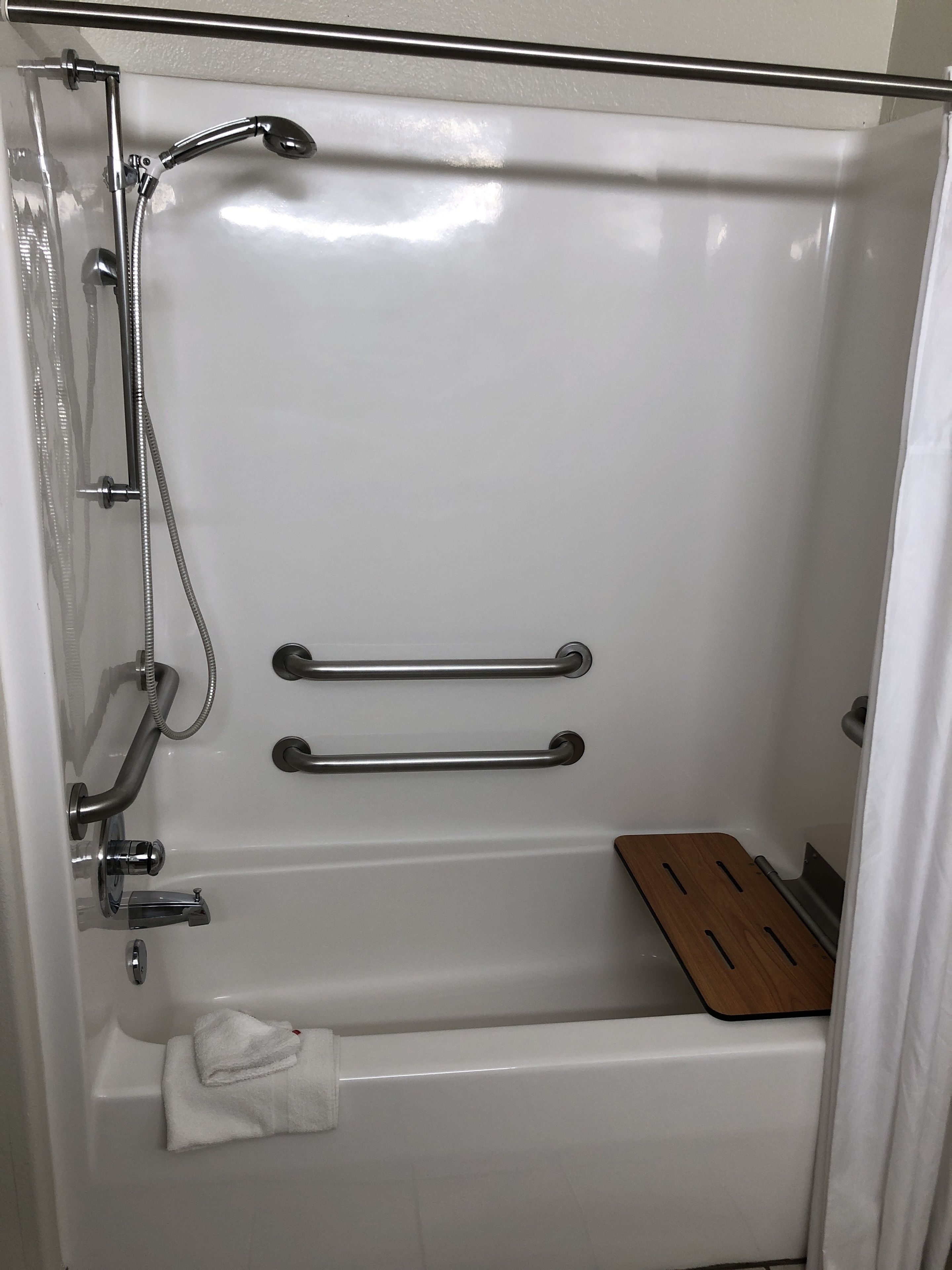 A white bathtub with a showerhead, grab bars, and a wooden seat.