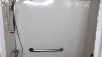 A white bathtub with a showerhead, grab bars, and a wooden seat.