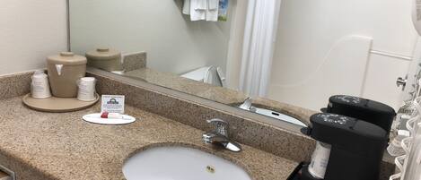 A hotel bathroom with a granite countertop, a sink, a mirror, a towel rack, and a coffee machine.