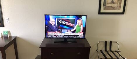 A television on a wooden cabinet displaying a news program.