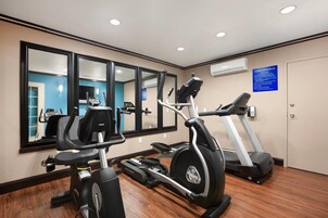 Un gimnasio con máquinas de cardio, espejos y un cartel azul con normas.