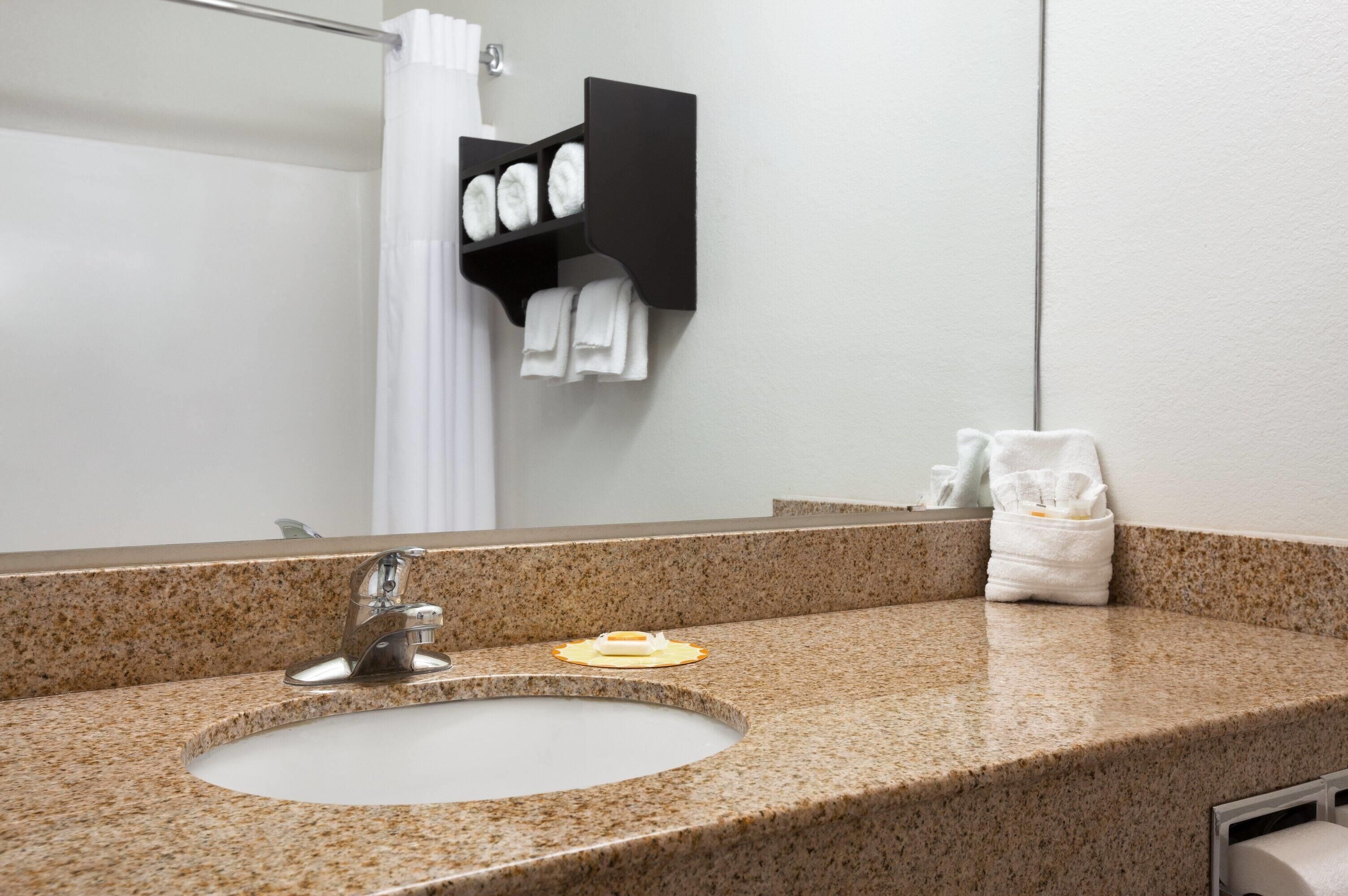 Une salle de bain avec un lavabo doté d’un plan de travail en granit, un miroir, un porte-serviettes avec des serviettes et un porte-savon.