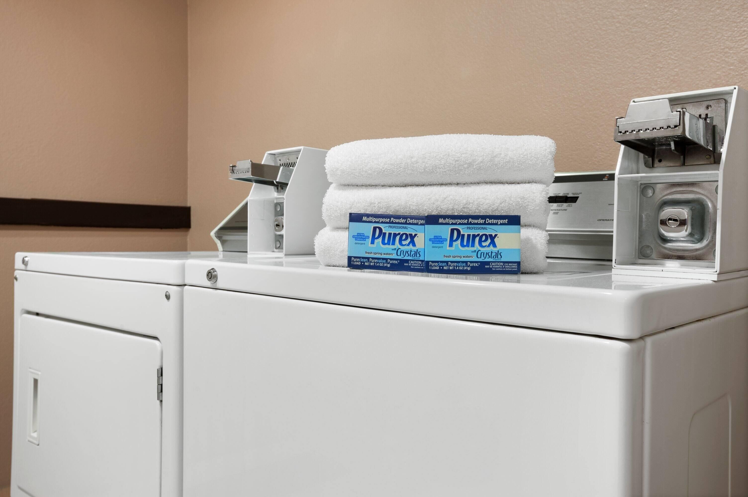 A front-loading washing machine with a white towel and a box of Purex detergent on top.