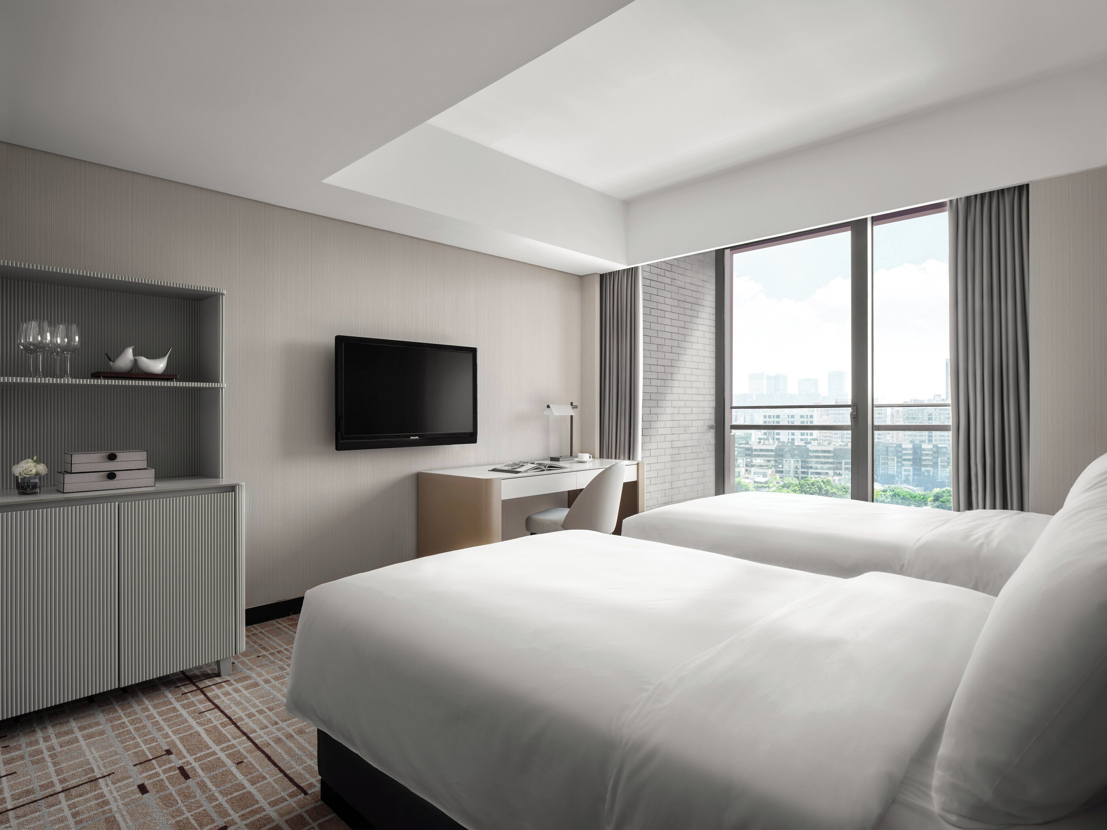 Una habitación de hotel moderna con una cama grande, un escritorio, un televisor de pantalla plana y vistas a la ciudad.