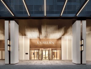 A modern hotel entrance with a prominent 'CORDIS' sign, a glass door entrance, and a decorative light installation above. - Cordis, Foshan, Lingnan Xintiandi (Foshan)