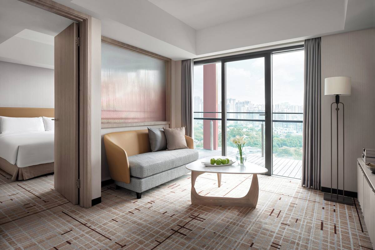 Moderni hotellihuone, jossa on sänky, sohva ja pöytä, jonka päällä on maljakko täynnä kukkia.