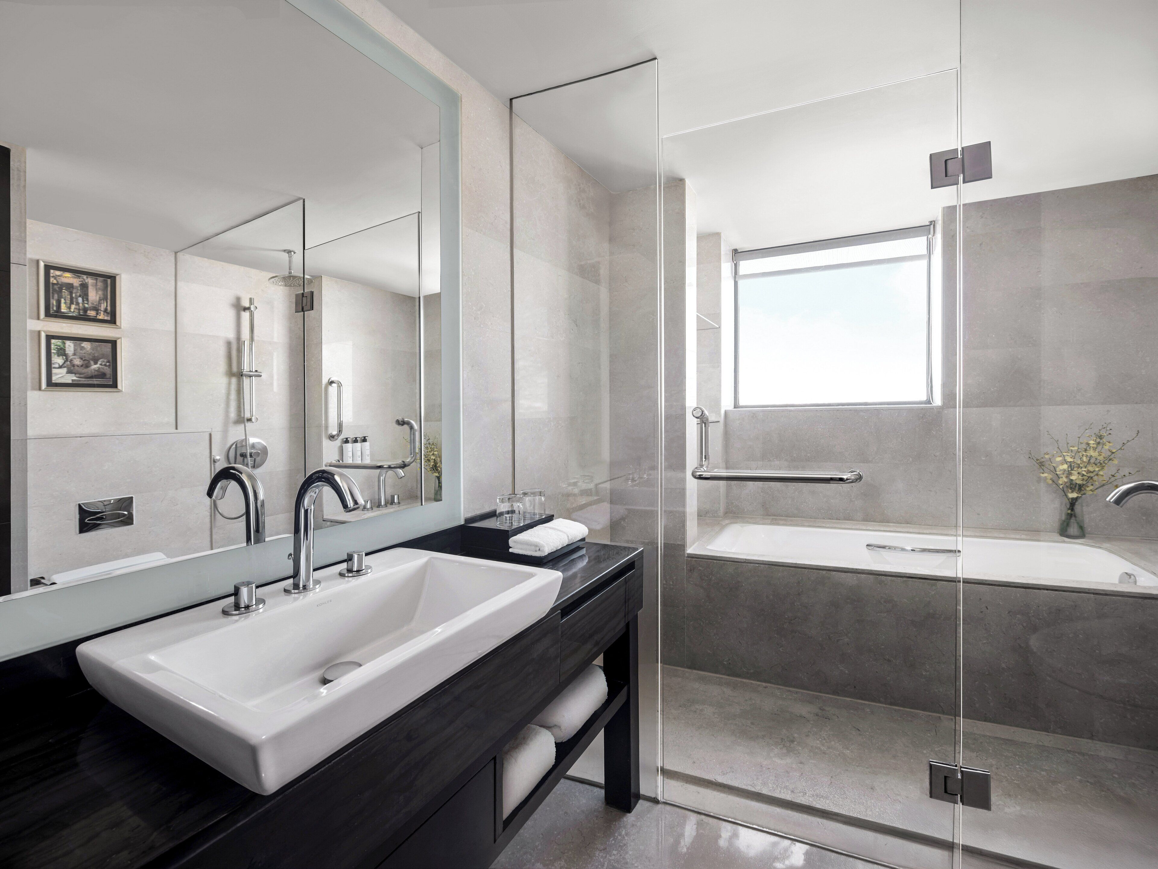 Un baño moderno con un espejo grande, un lavamanos blanco, un mueble de tocador negro y una zona de ducha con mampara de cristal.