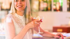 A person holding a cocktail glass with a lemon slice, standing in a bar with bottles in the background. - Novotel Constantine (Constantine)