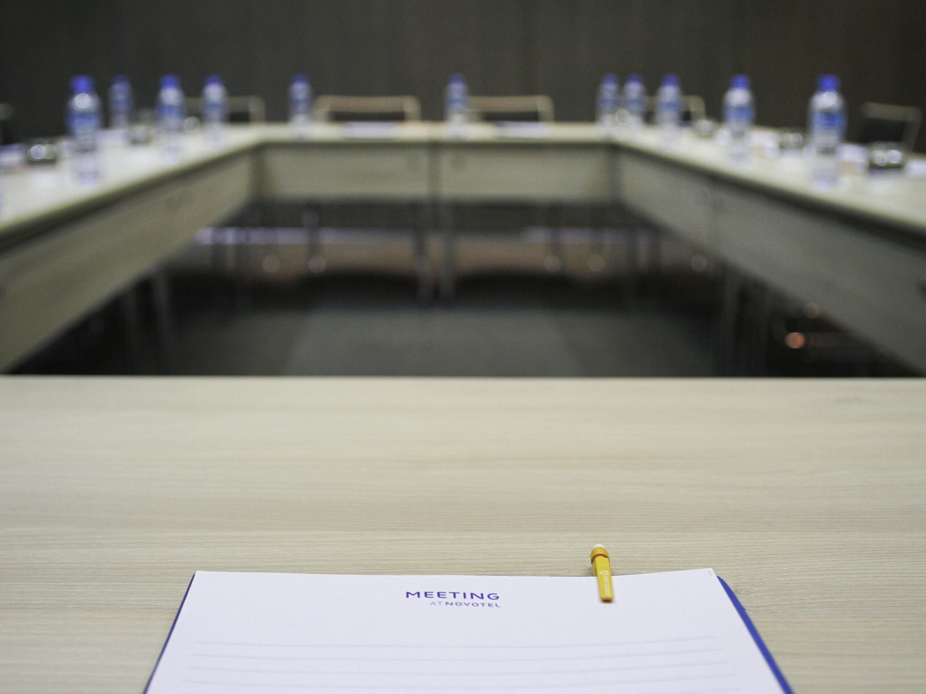 Una mesa de reuniones con botellas de agua y un bloc de notas que dice 'REUNIÓN MEDIODÍA VOTEL'.