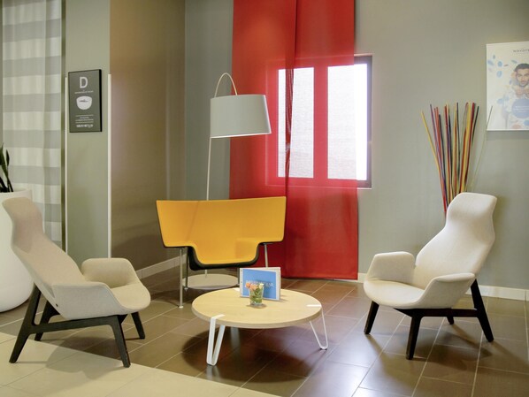 A modern room with two white armchairs, a yellow chair, a round table, a floor lamp, and a window with red curtains.