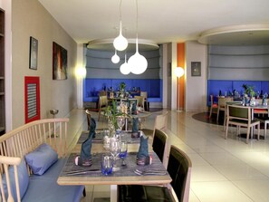 A modern dining area with round tables, blue upholstered seating, and pendant lighting.