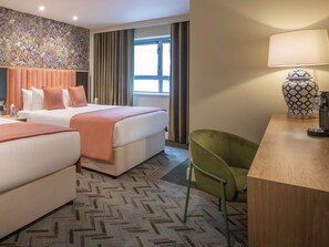 A hotel room with two beds, a green chair, a lamp, and a window with curtains. - Hyde Hotel (Galway)