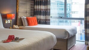 A hotel room with two beds, a desk with a laptop, a chair, and a view of the city. - Hyde Hotel (Galway)