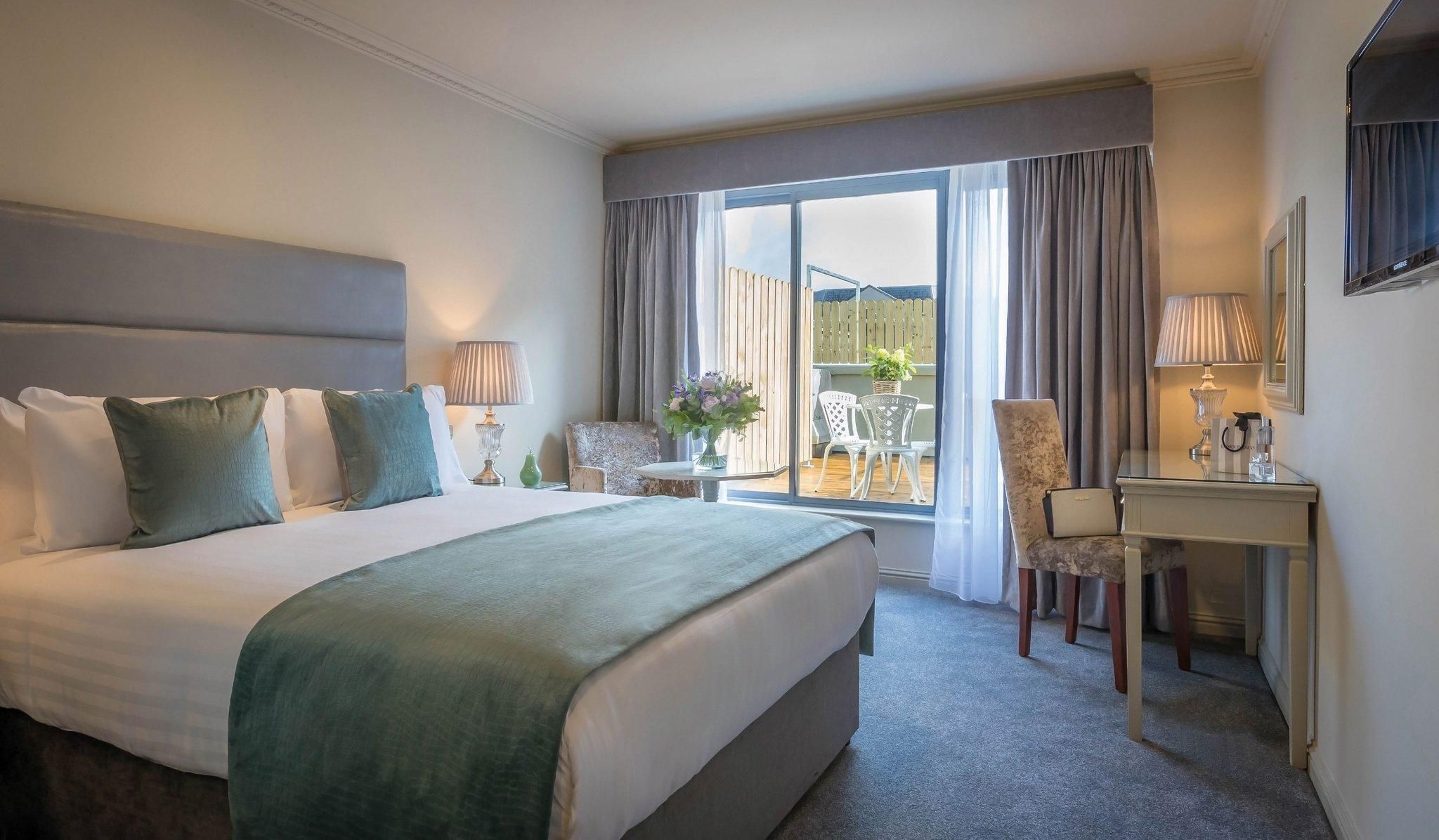 A hotel room with a bed, a desk, a chair, a small table, and a view of the outside.