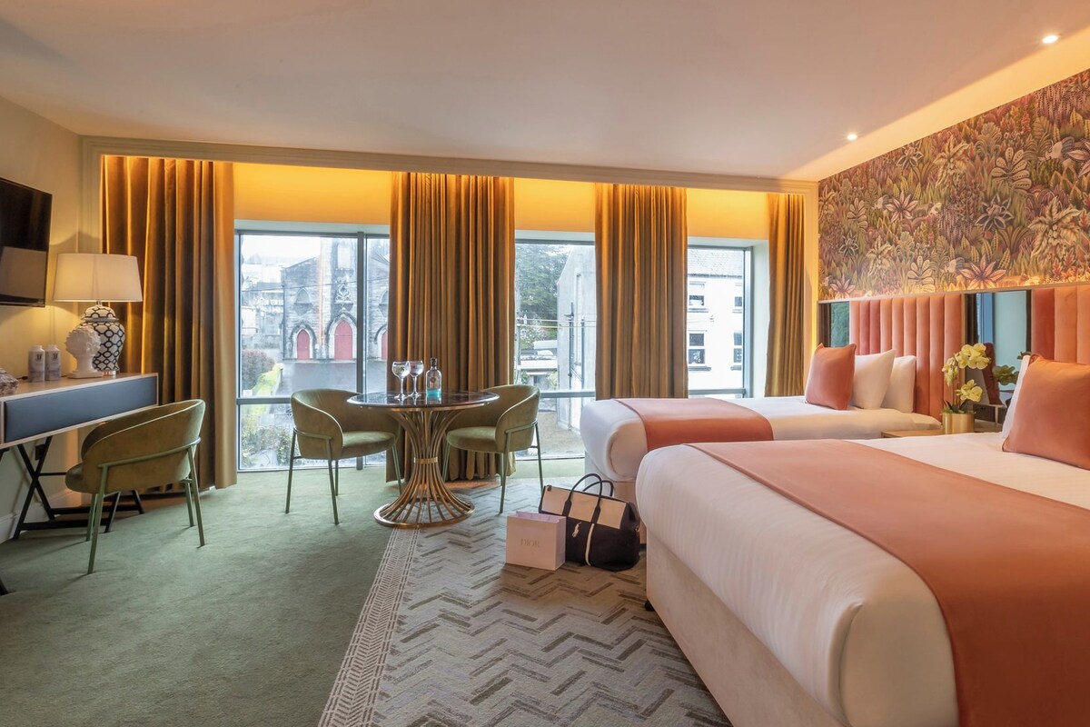 A hotel room with a bed, a desk, a chair, a table, and a view of the city.