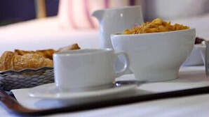 A breakfast tray with a bowl of cereal, a cup, and a small bowl on a bed with a striped pillow and a lamp in the background. - Hyde Hotel (Galway)