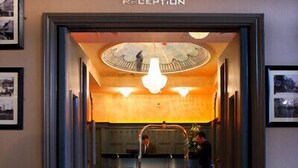 A reception area with a sign above the door, a counter, and a person standing by the counter. - Hyde Hotel (Galway)