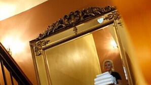 A staircase with ornate railings and a large mirror reflecting a person carrying a white object. - Hyde Hotel (Galway)