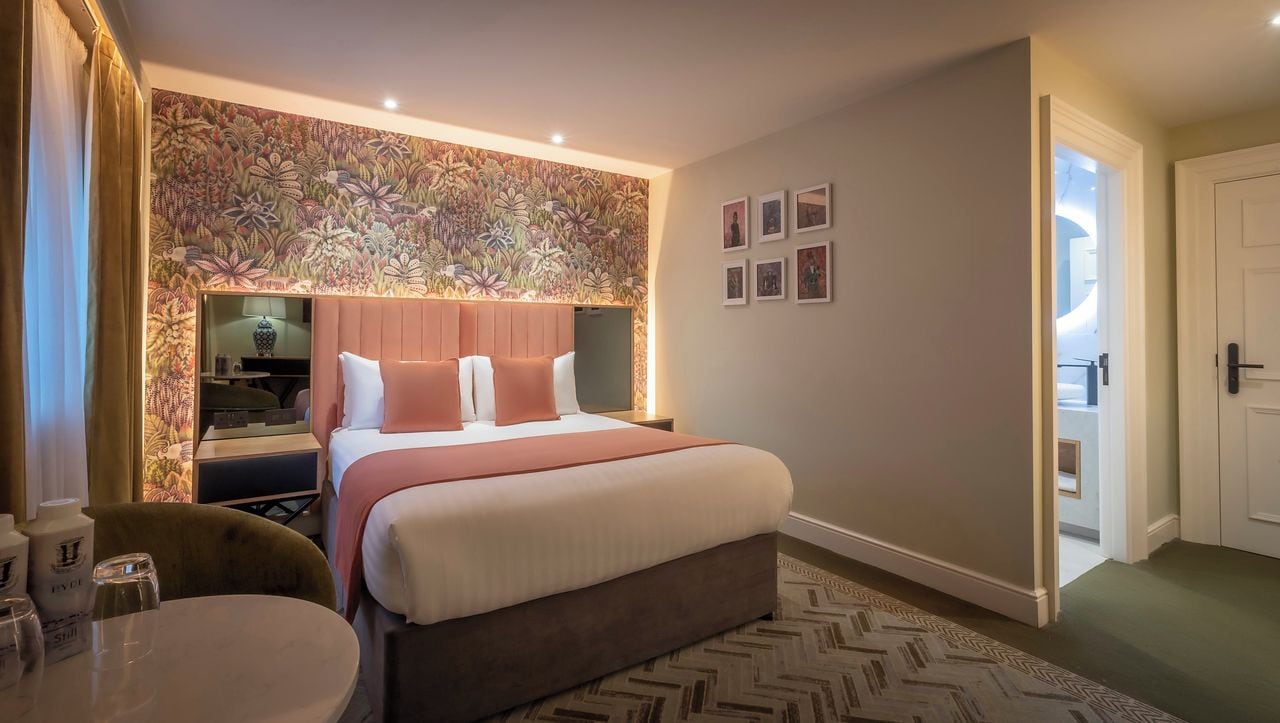 Een hotelkamer met een groot bed, een nachtkastje met een lamp, een stoel en een klein tafeltje met glazen.