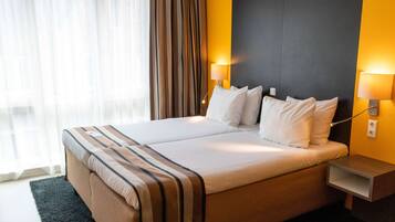 A double bed with a striped bedspread, two bedside lamps, a nightstand, and a view of a window with curtains.