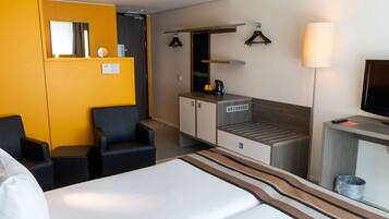 Una habitación de hotel con cama, escritorio, silla, kitchenette pequeña y televisión.