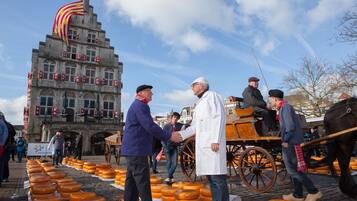 A historic building with a large flag, a horse-drawn carriage, and a display of cheese wheels.
