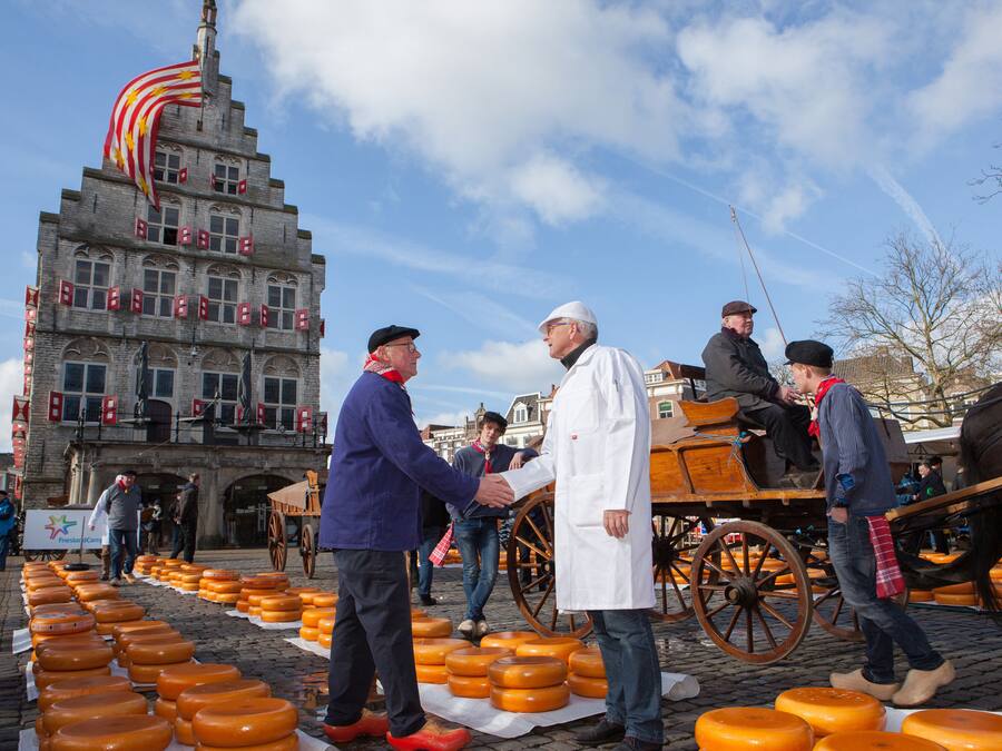 Un edificio histórico con una gran bandera, un carruaje tirado por caballos y una exhibición de ruedas de queso.