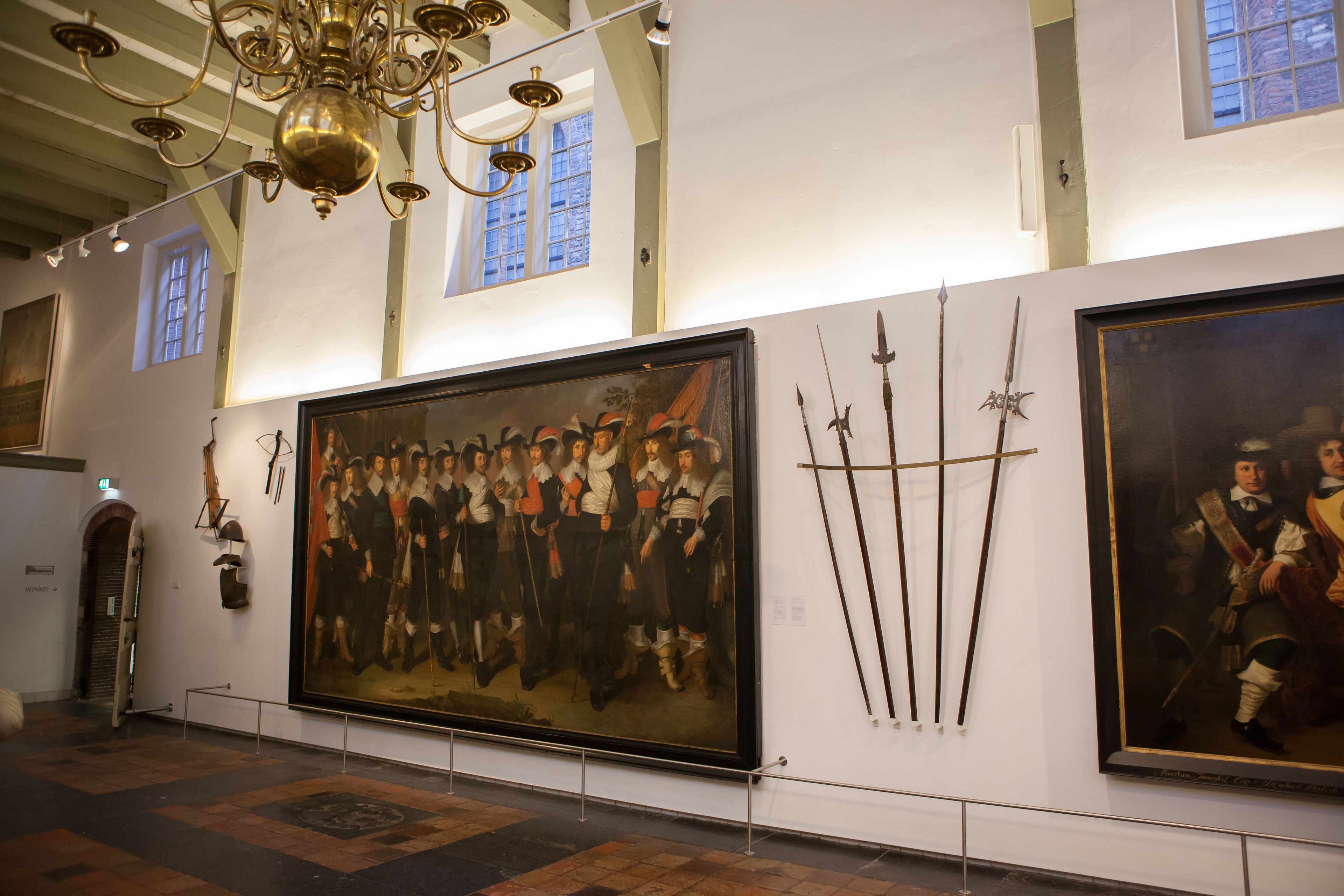 Ein Museuminnenraum mit einem großen Gemälde, historischen Artefakten und einer Kristallleuchter.