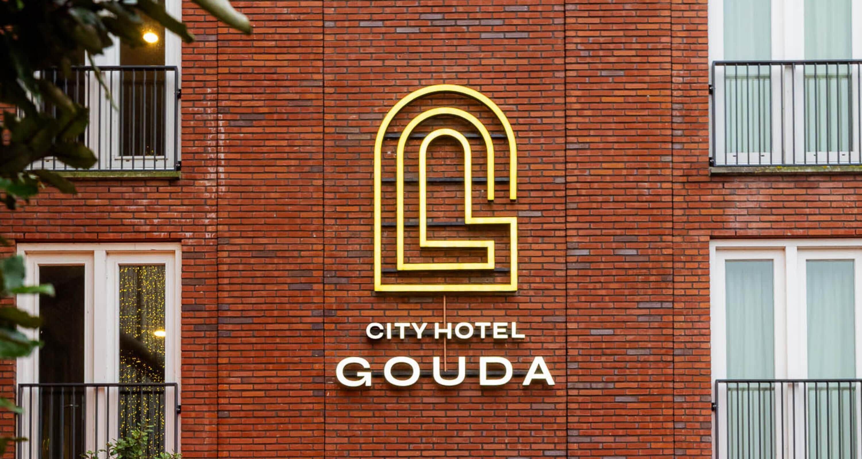 Un edificio de ladrillo con un gran logotipo iluminado con una 'G' y el texto 'CITY HOTEL GOUDA' en la fachada.