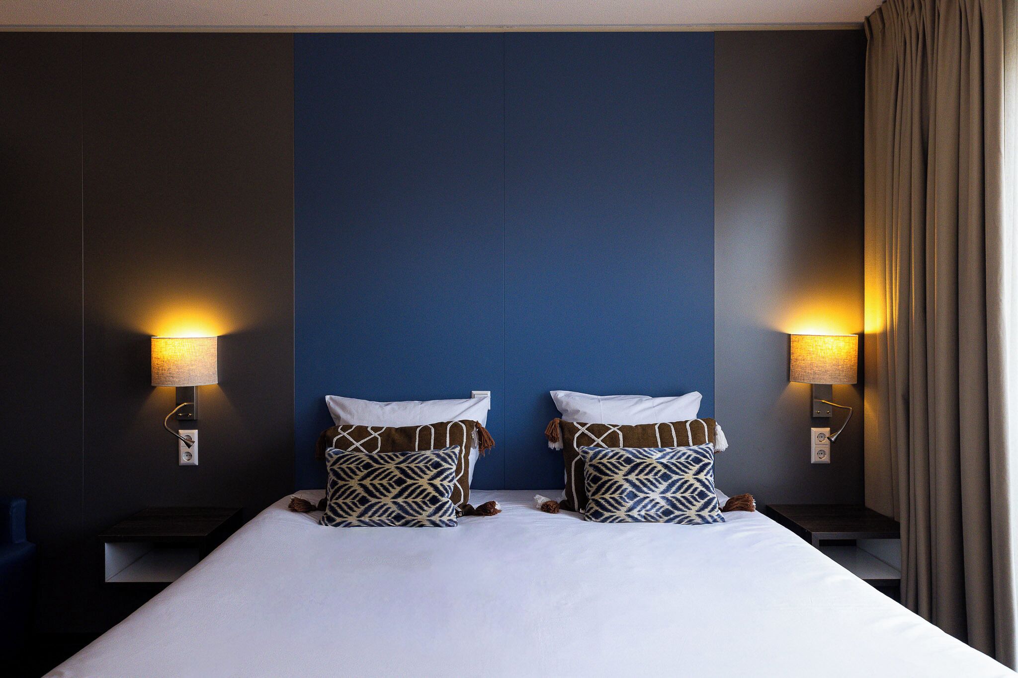 Una habitación de hotel con una cama grande, dos lámparas de noche y una pared azul decorativa.