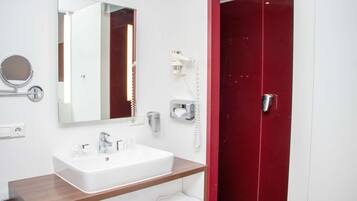 A modern bathroom with a white sink, a mirror, a hairdryer, and a red door.