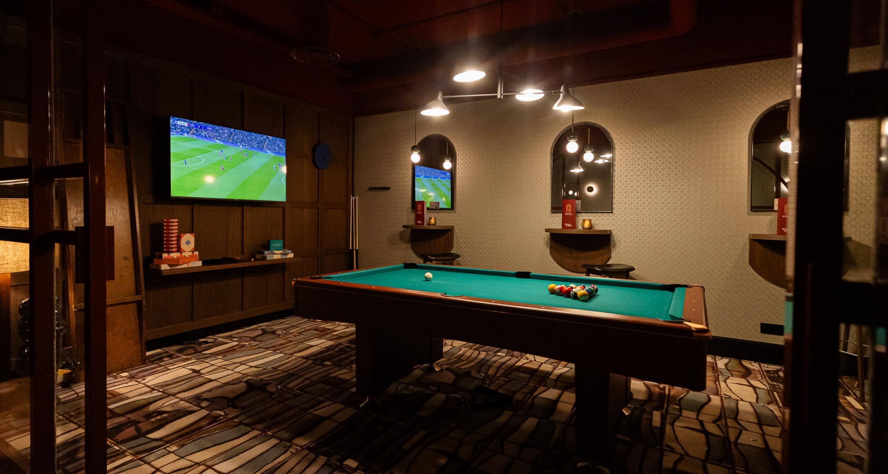 A pool table with a billiard ball, a television displaying a sports game, and a bar area with stools.