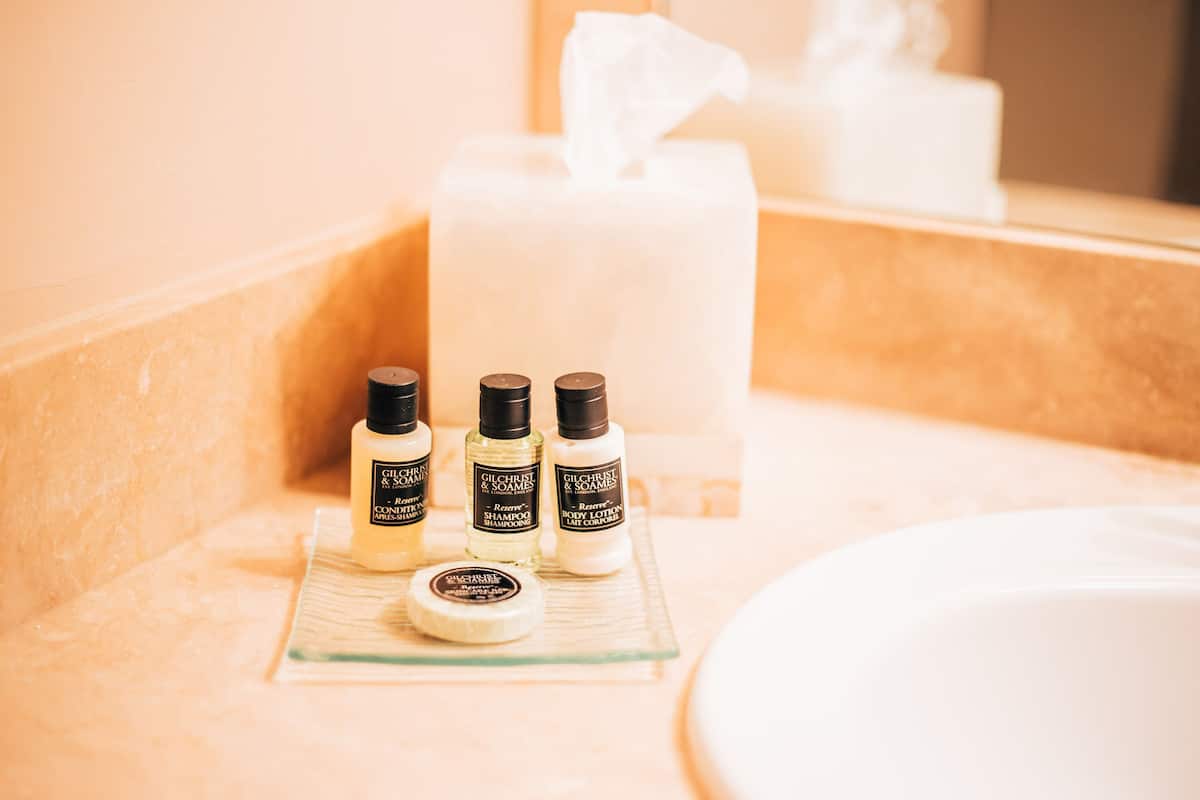 Een badkamermeubel met een glazen zeepbakje, drie flesjes Gilchrist & Soame body lotion en een witte kaars.