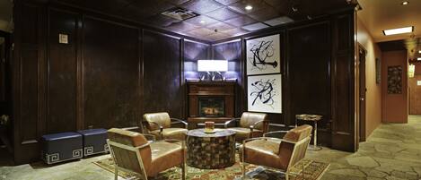 A lobby with leather chairs, a round coffee table, a fireplace, and artwork on the walls.