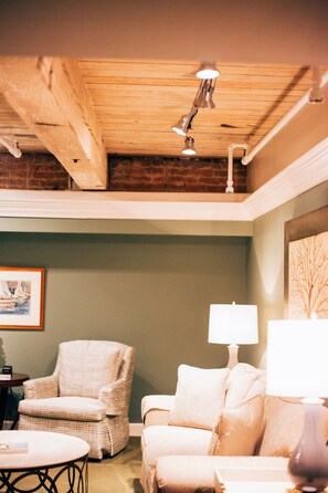 A cozy room with a wooden ceiling, a checkered armchair, a sofa, a table, and a lamp.